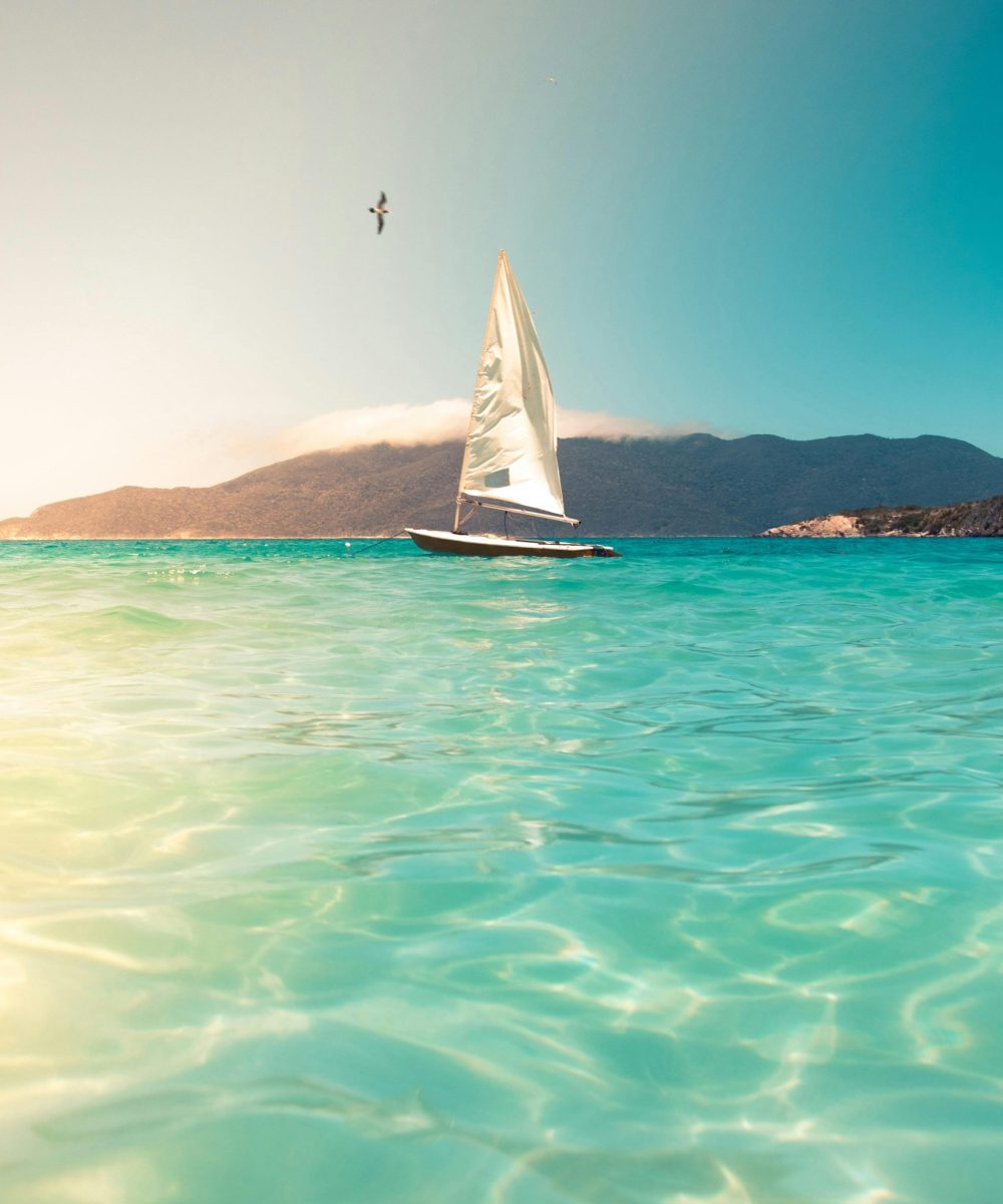A sailboat glides across turquoise seas beneath a clear sky, ideal for tranquil travel and vacation scenes.