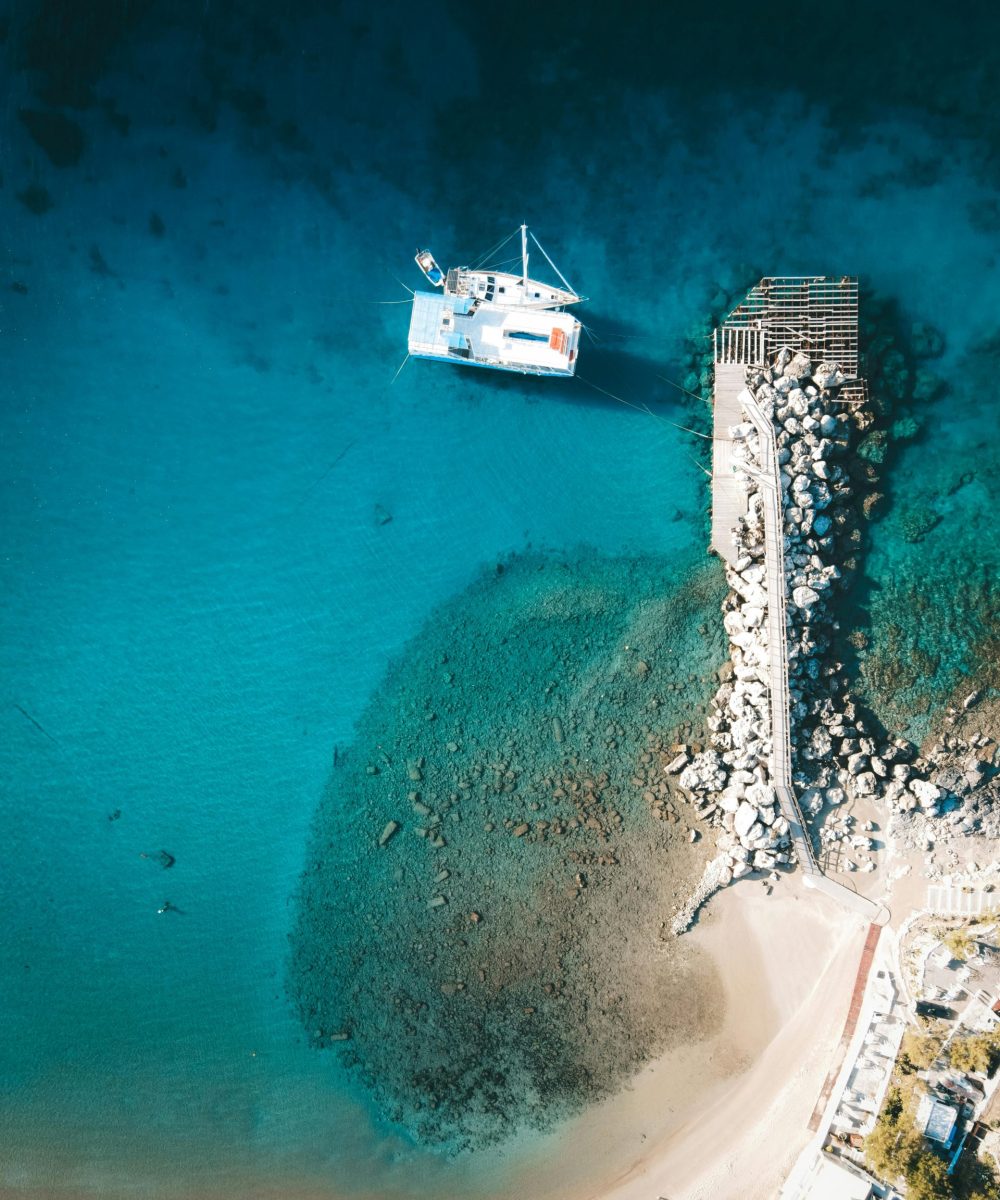 Stunning aerial shot of a catamaran docked at Lindos, Greece, with turquoise waters and rocky pier.