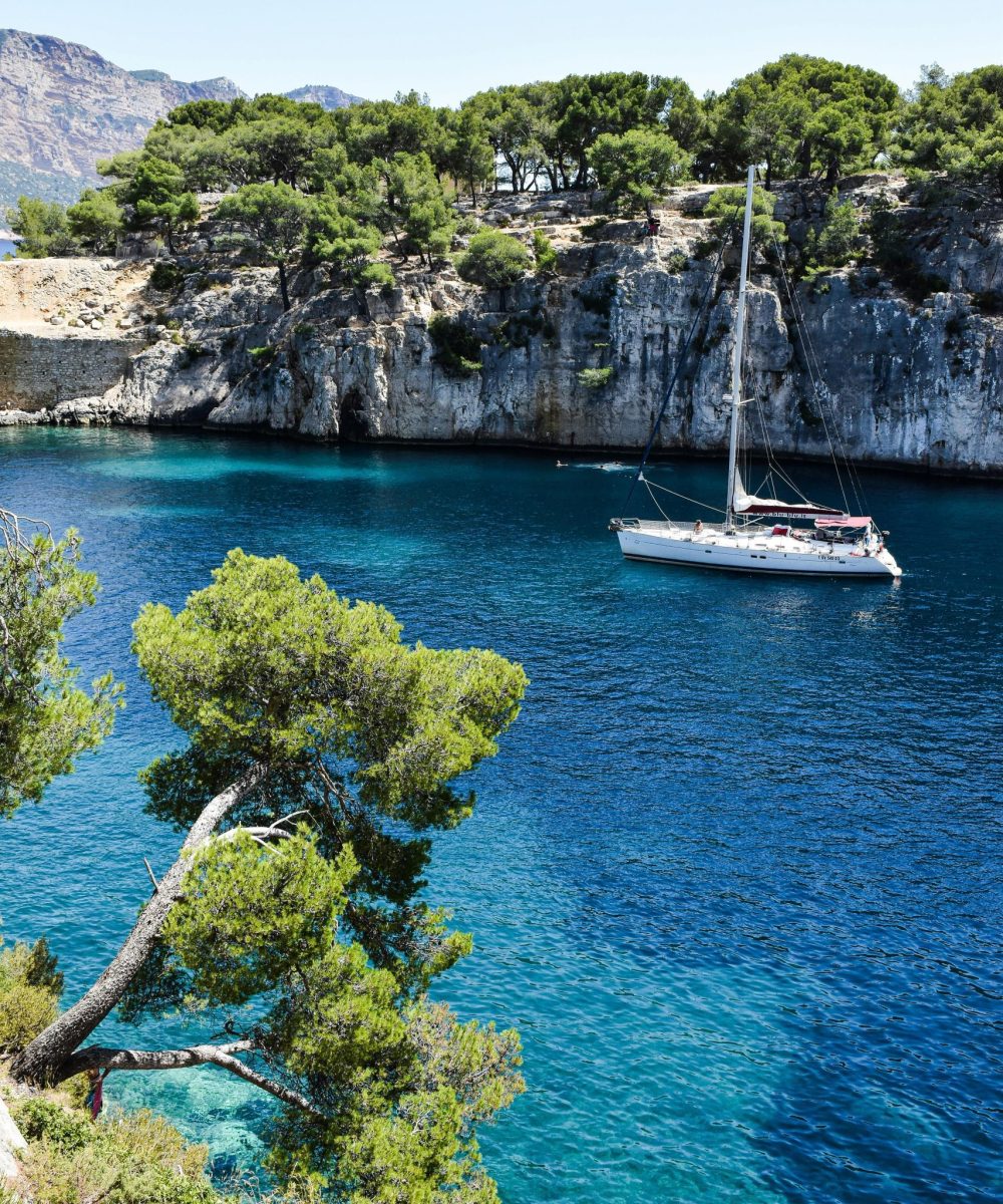 Stunning sailboat sailing in crystal clear waters of Calanques, France, surrounded by lush green cliffs.