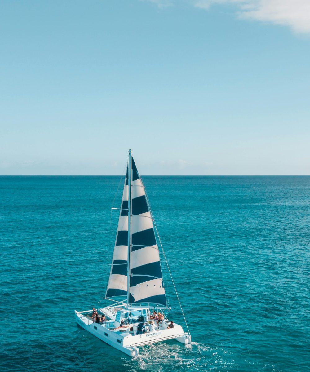 A sailboat with people cruising on a tranquil, open blue sea under a clear sky.